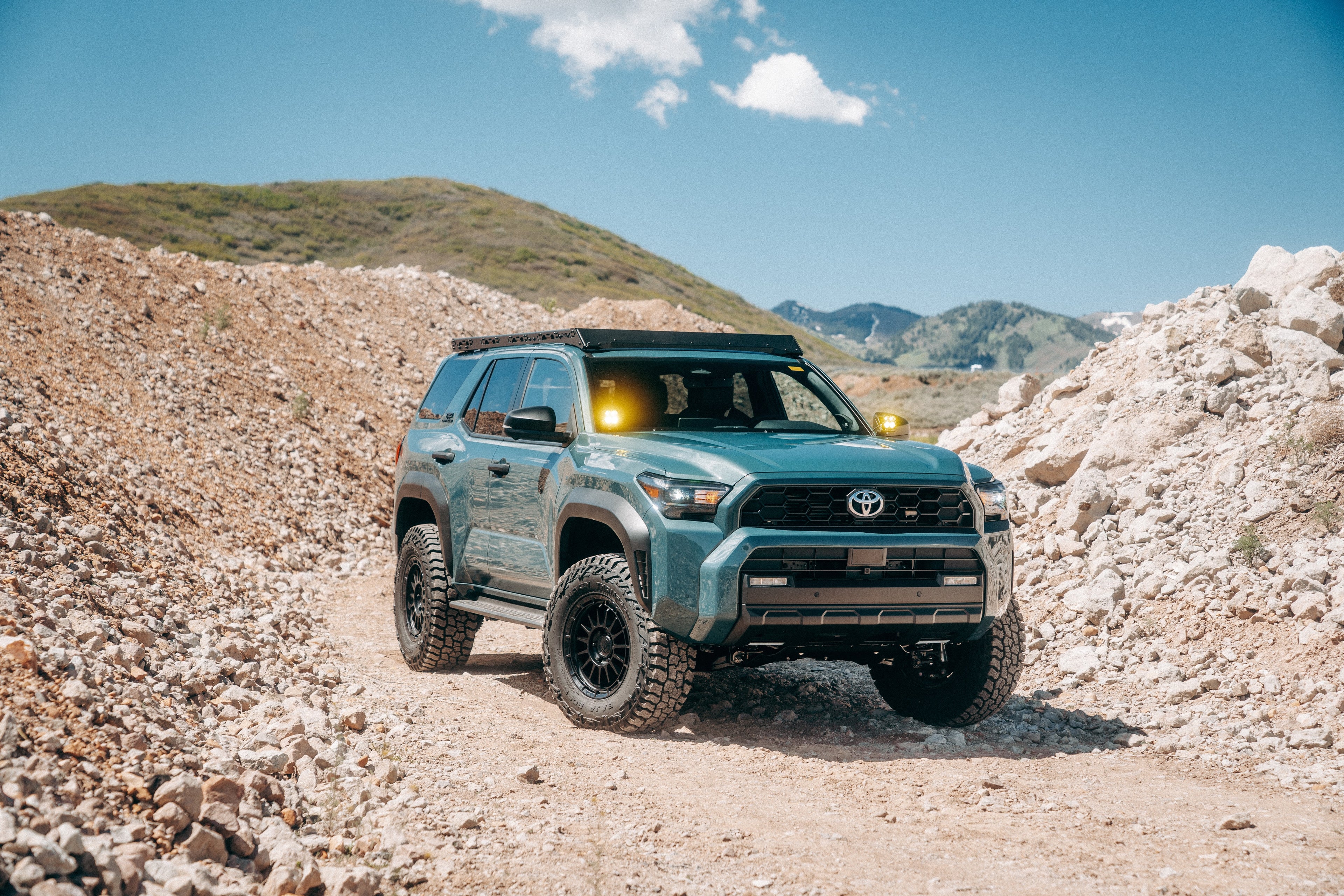 2026 Toyota 4Runner on a rocky trail with mountains in the background with Icon suspension, Fuel wheels, Mickey thompson tires, DV8 roof rack and Baja Designs lights